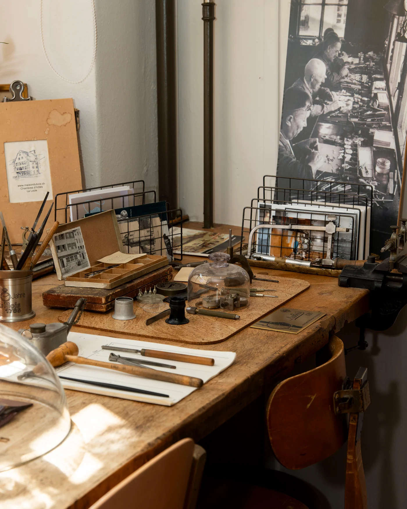 Un établi de la maison avec des outils horlogers et une photographie ancienne des artisans au travail