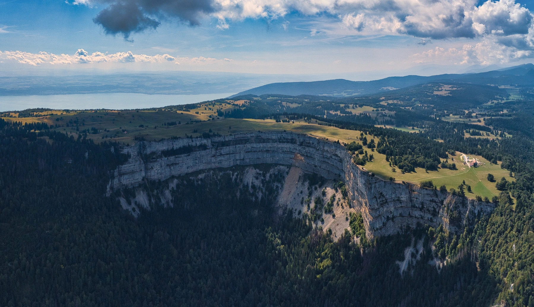 Vue aérienne du Creux du Van en été, avec le lac de Neuchâtel à l’arrière-plan